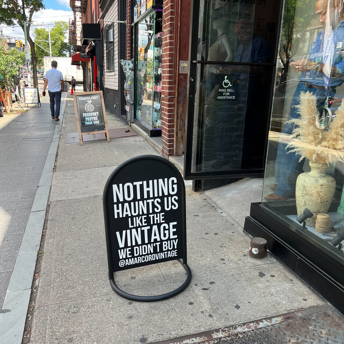 Black rounded sidewalk sign with Nothing Haunts Us Like the Vintage We Didn't Buy lettering.
