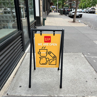 Yellow SIP coffee sign in a black sidewalk frame.