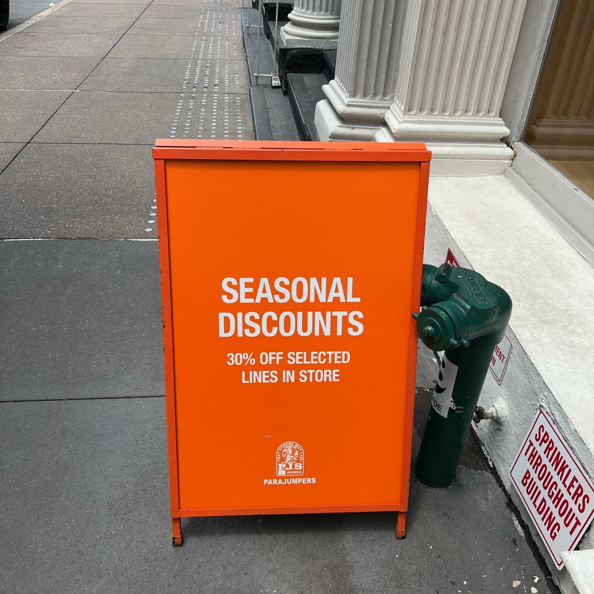 Orange Parajumpers sidewalk sign advertising seasonal discounts.
