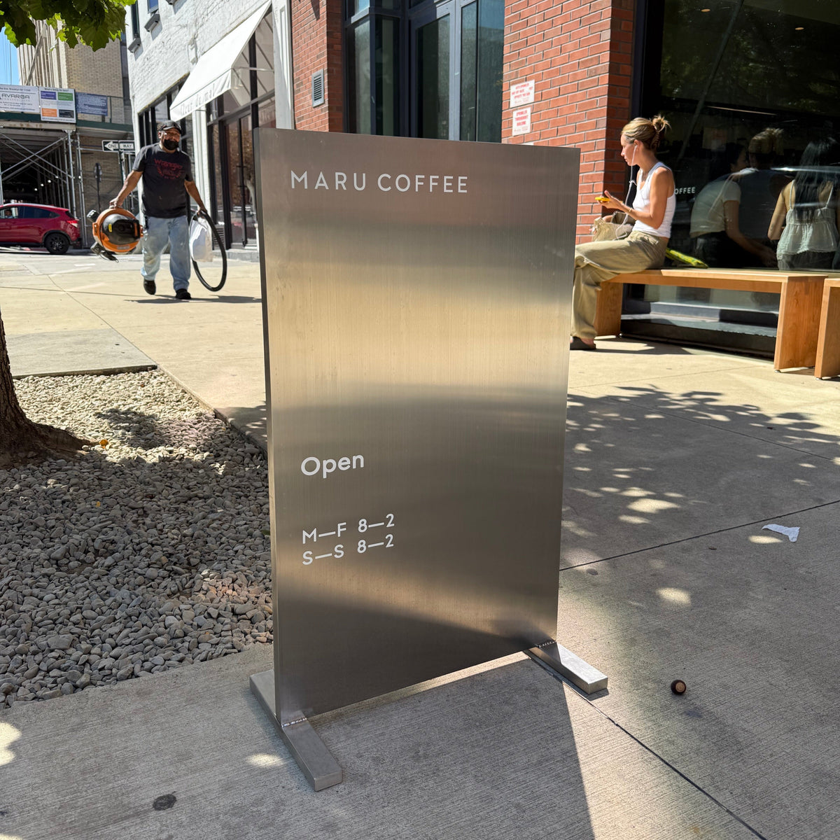 Brushed stainless steel upright sign with Maru Coffee lettering outside a café.