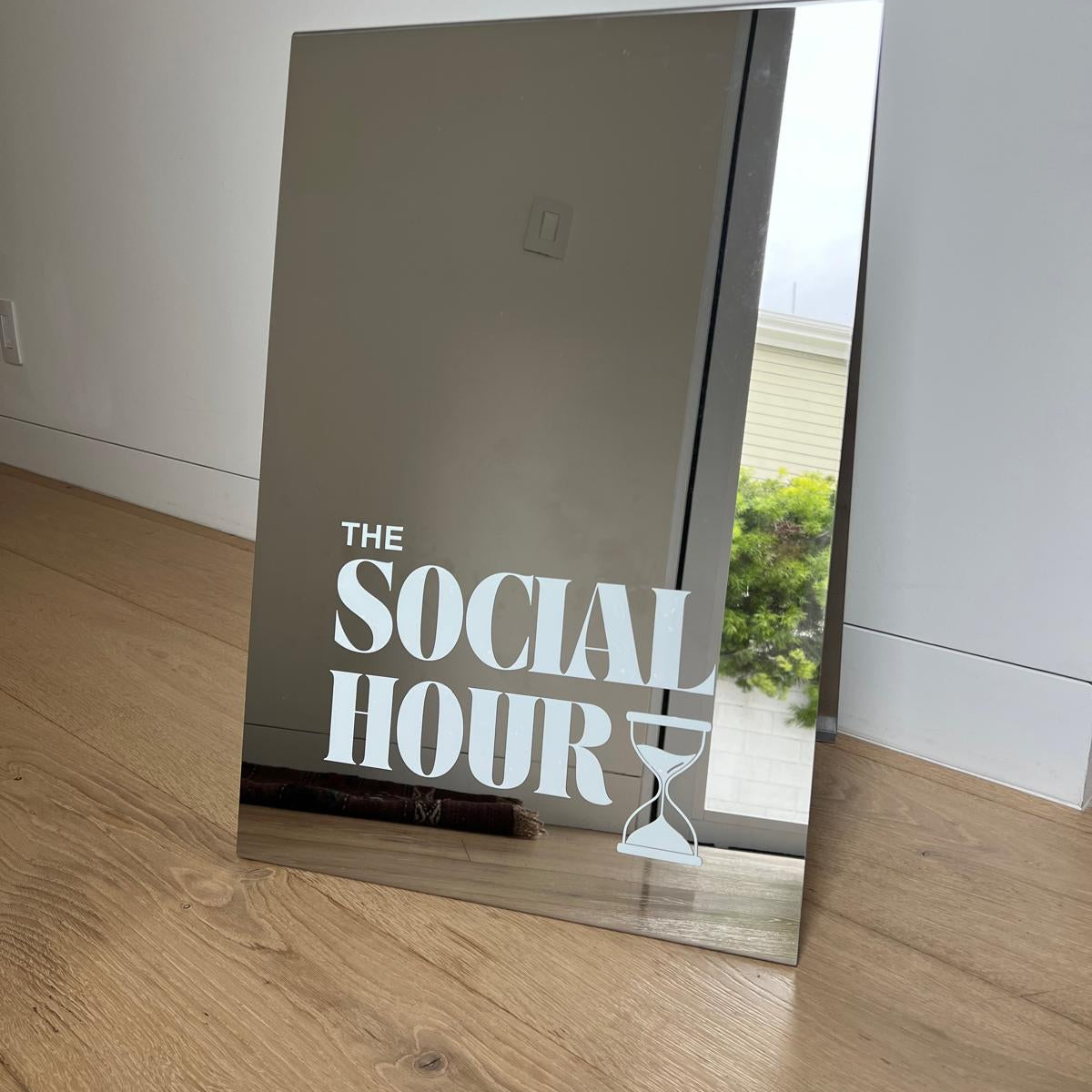 Mirrored rectangular sign with The Social Hour lettering, leaning against a wall.