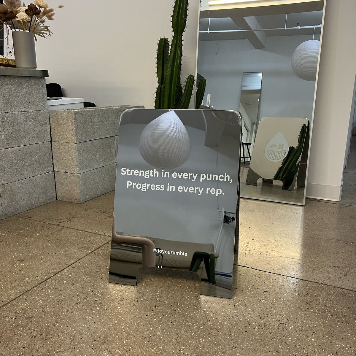 Mirrored A-frame sign with white printed lettering displayed indoors.