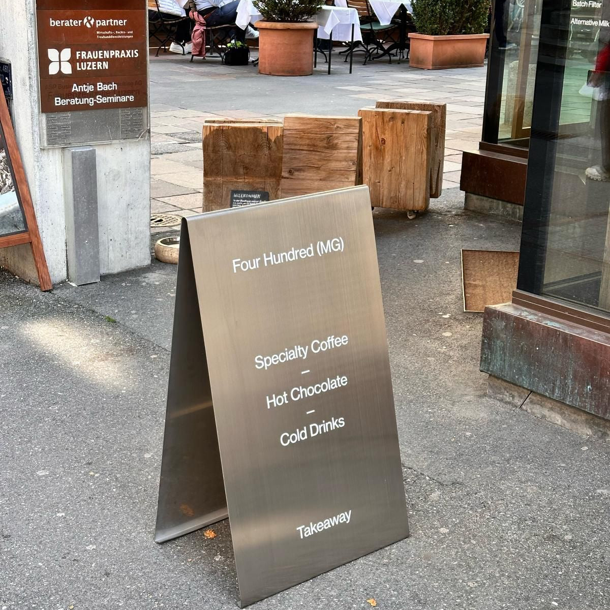 Brushed metal A-frame sign with white service lettering outside a storefront.