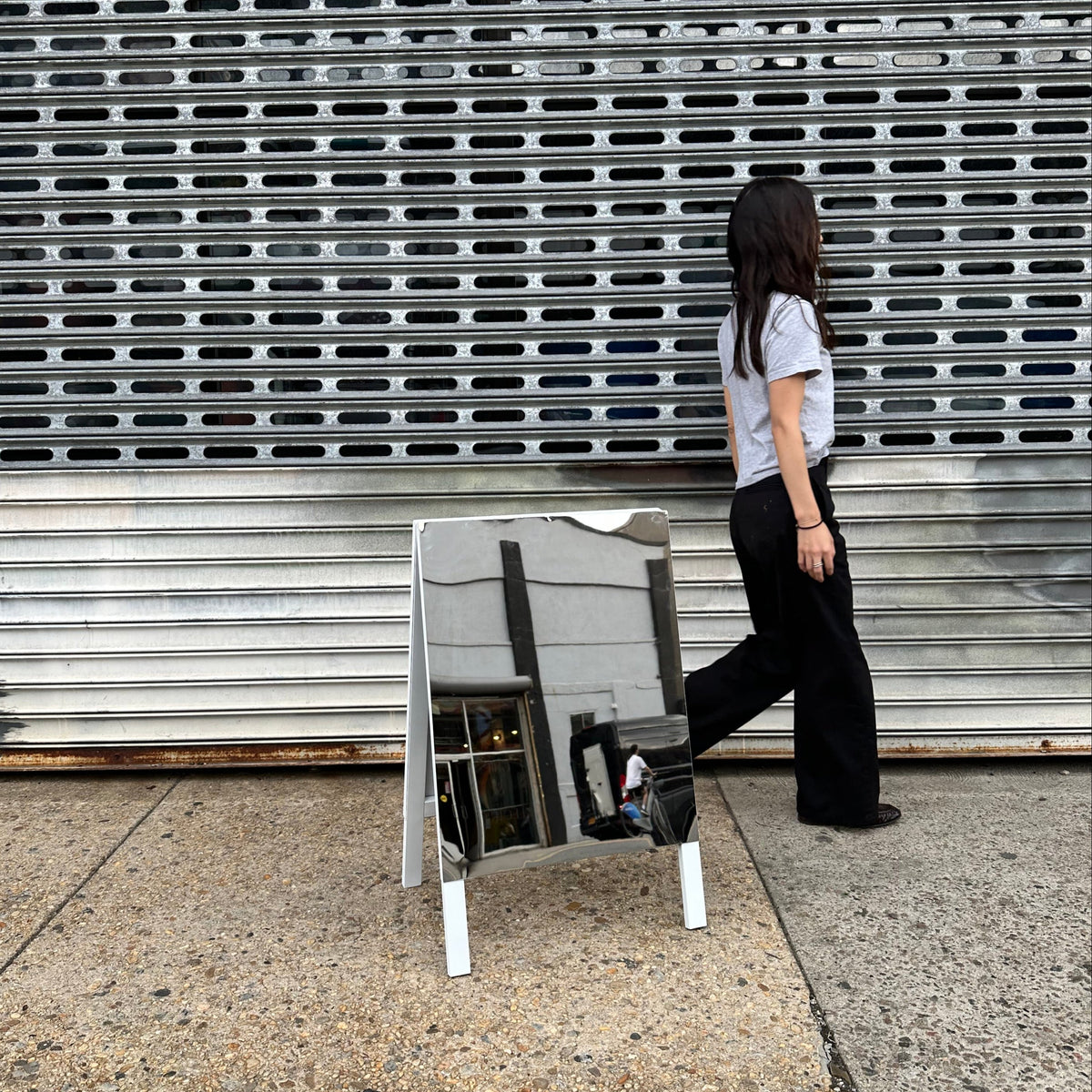 Person walking beside a mirrored A-frame sign with white legs.