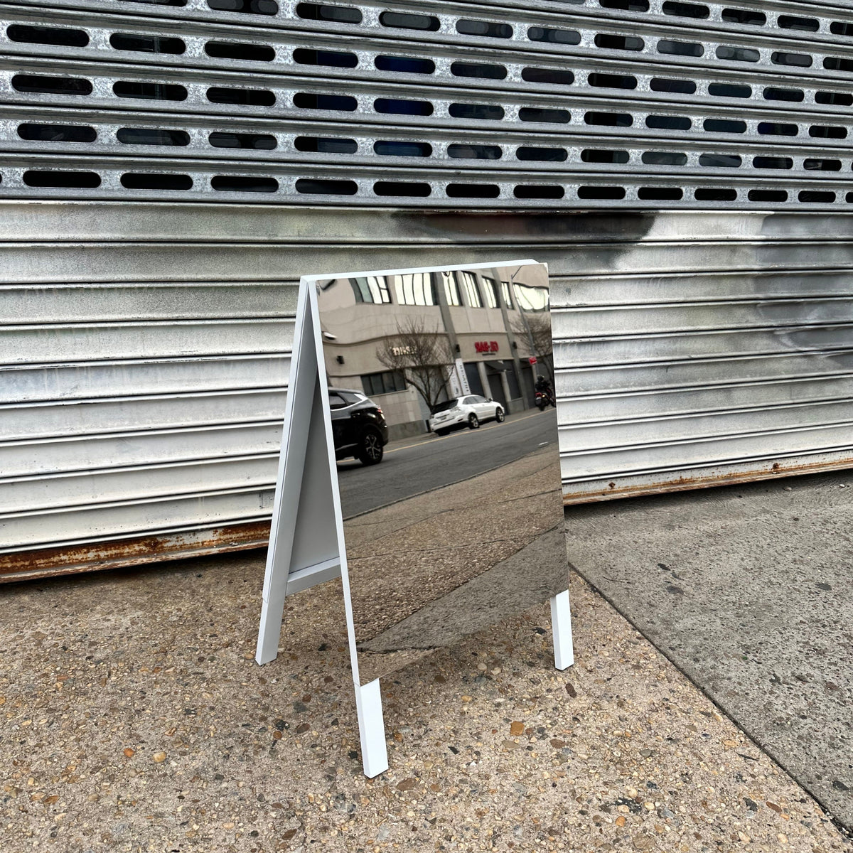 Angled view of a mirrored A-frame sign showing its white legs and folding sides.