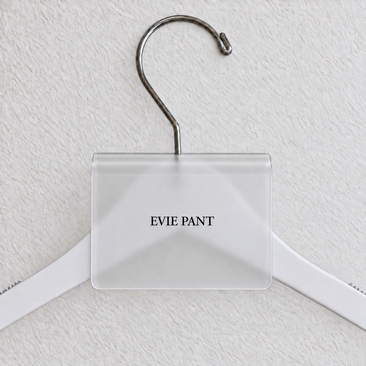 Clear Matte acrylic hanger sign clip with soft edge reflections, resting on a white wooden hanger, with example EVIE PANT print
