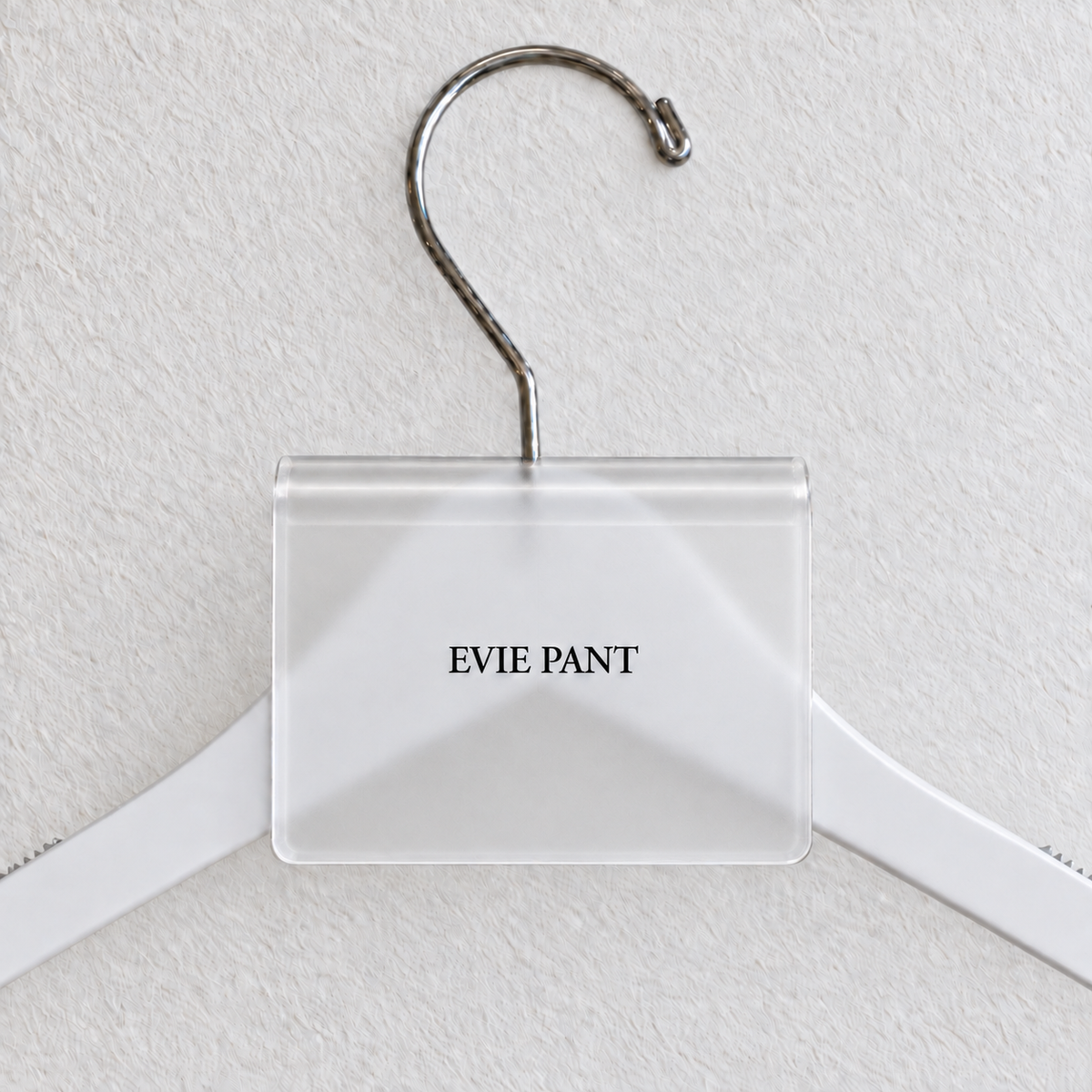 Clear Matte acrylic hanger sign clip resting on the rounded crown of a white wooden hanger, with example EVIE PANT print