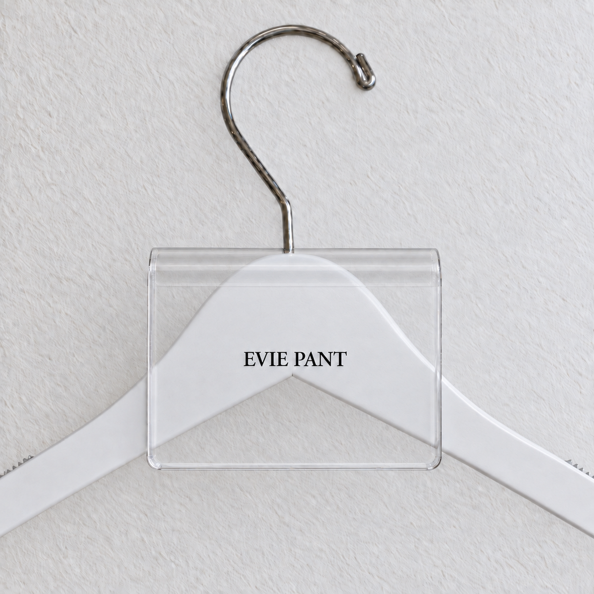 Clear acrylic hanger sign clip with soft edge reflections, resting on a white wooden hanger, with example EVIE PANT print