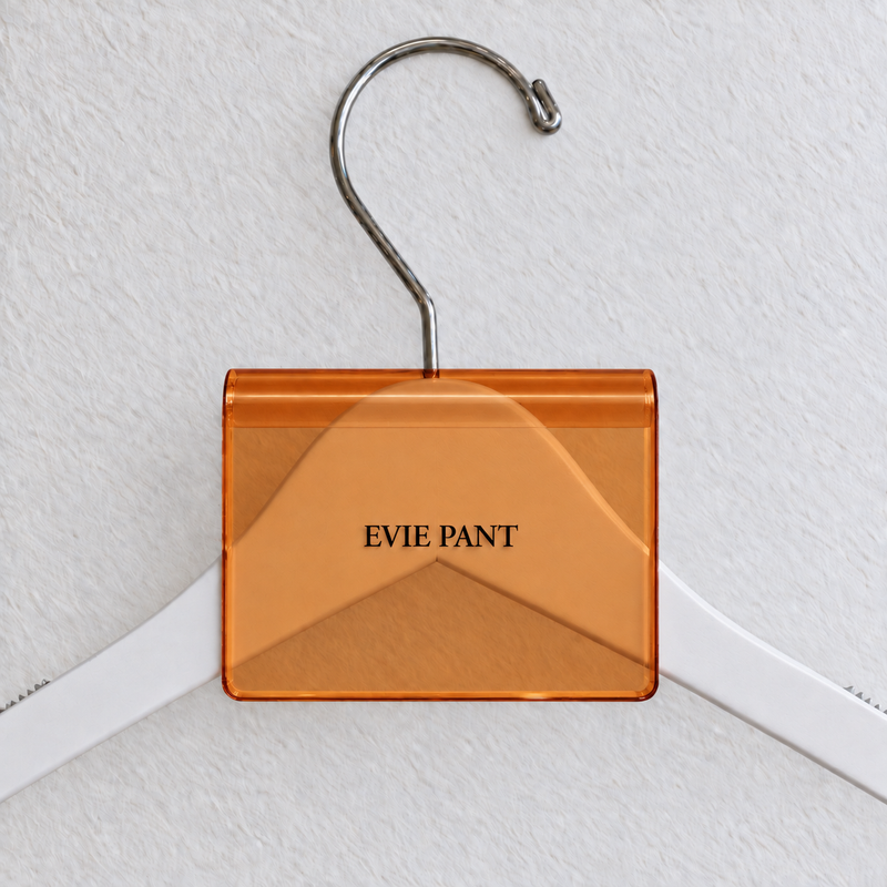 Orange transparent acrylic hanger sign clip with soft edge reflections, resting on a white wooden hanger, with example EVIE PANT print