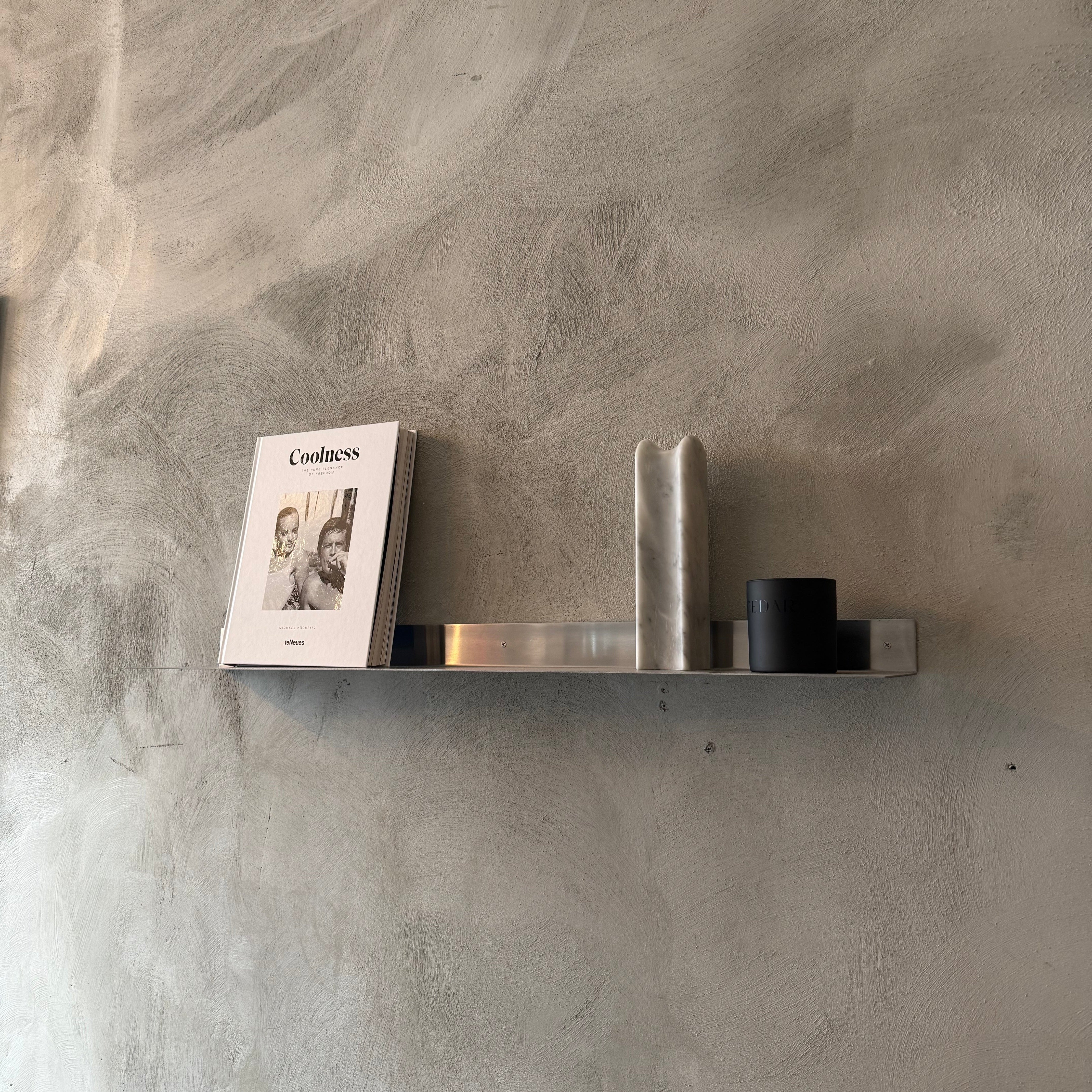 Metallic shelf against a textured gray wall with a book and small decorative item.