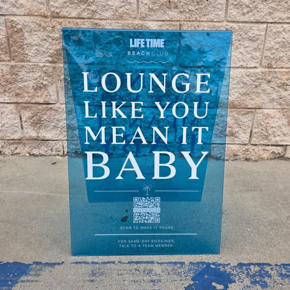 Blue transparent acrylic A-frame sign with Life Time Lounge Like You Mean It Baby lettering.