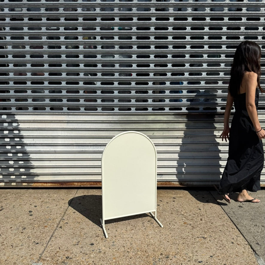 Person walking beside a cream arched standing sign, showing its scale.