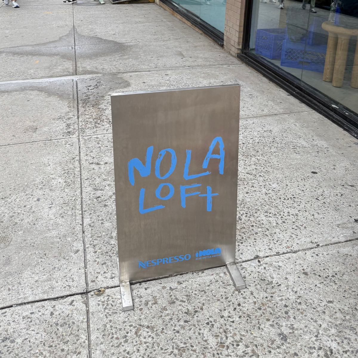 Stainless steel upright sign with blue Nola Loft lettering and an arrow.