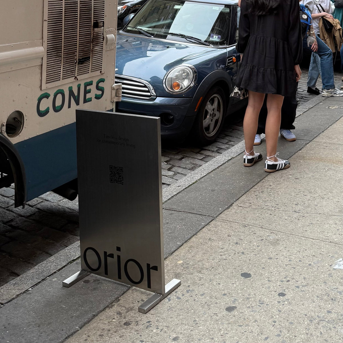 Stainless steel upright sign with Orior lettering beside a parked ice cream truck.