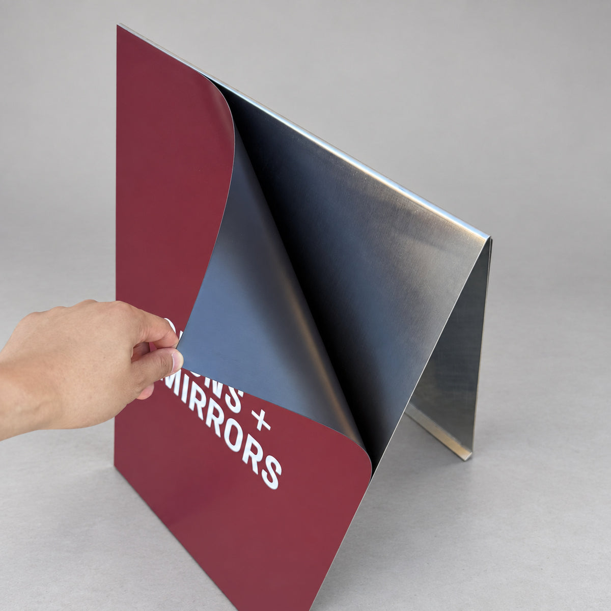 Hand peeling a removable burgundy magnetic cling from the #002M stainless steel A-frame sidewalk sign.