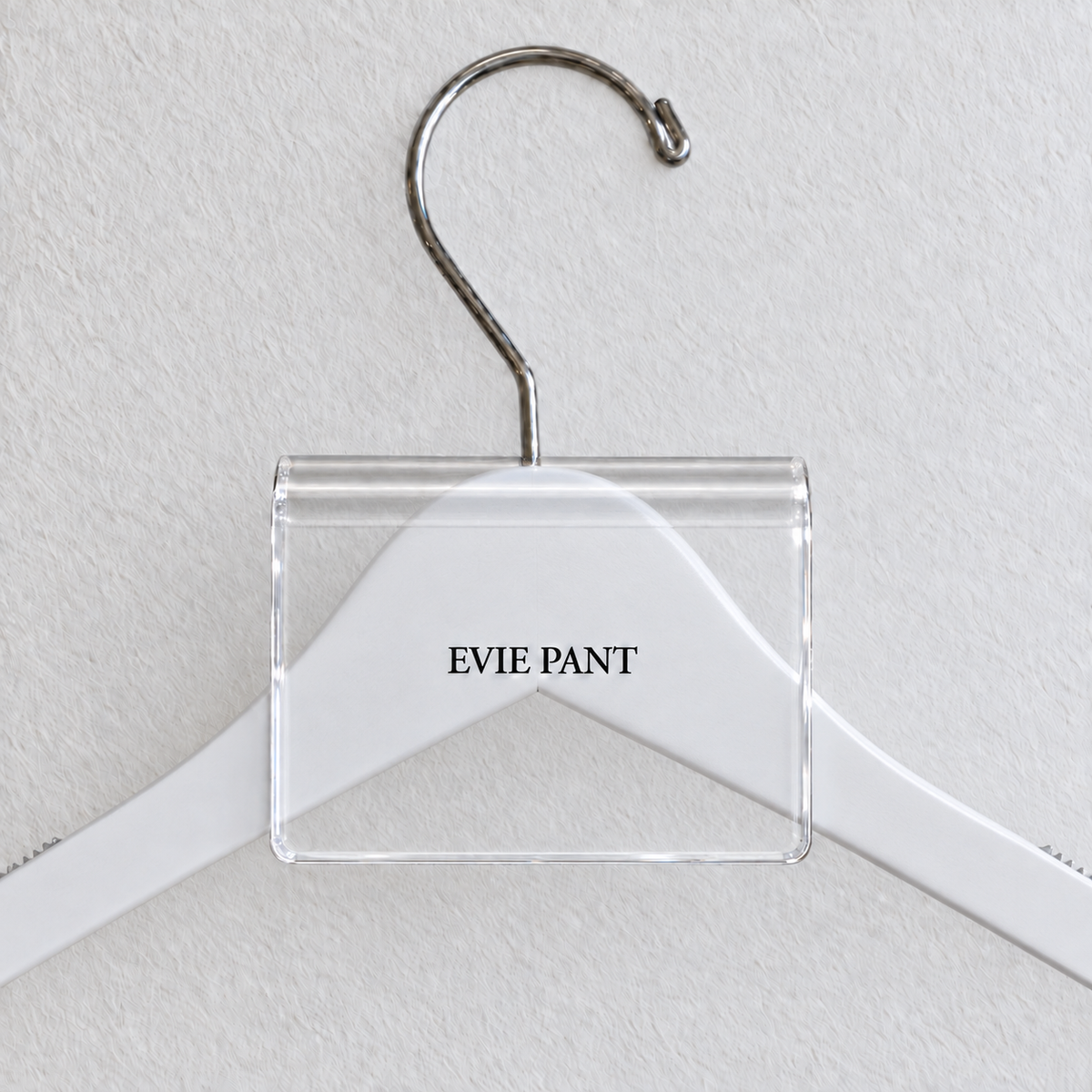 Clear acrylic hanger sign clip resting on the rounded crown of a white wooden hanger, with example EVIE PANT print