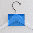 Dark Blue acrylic hanger sign clip resting on the rounded crown of a white wooden hanger, with example EVIE PANT print