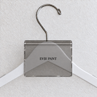 Gray Smoke acrylic hanger sign clip resting on the rounded crown of a white wooden hanger, with example EVIE PANT print