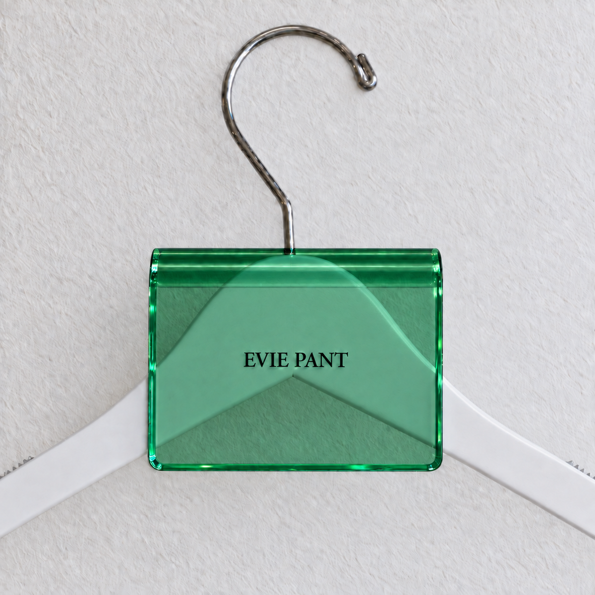 Green acrylic hanger sign clip resting on the rounded crown of a white wooden hanger, with example EVIE PANT print