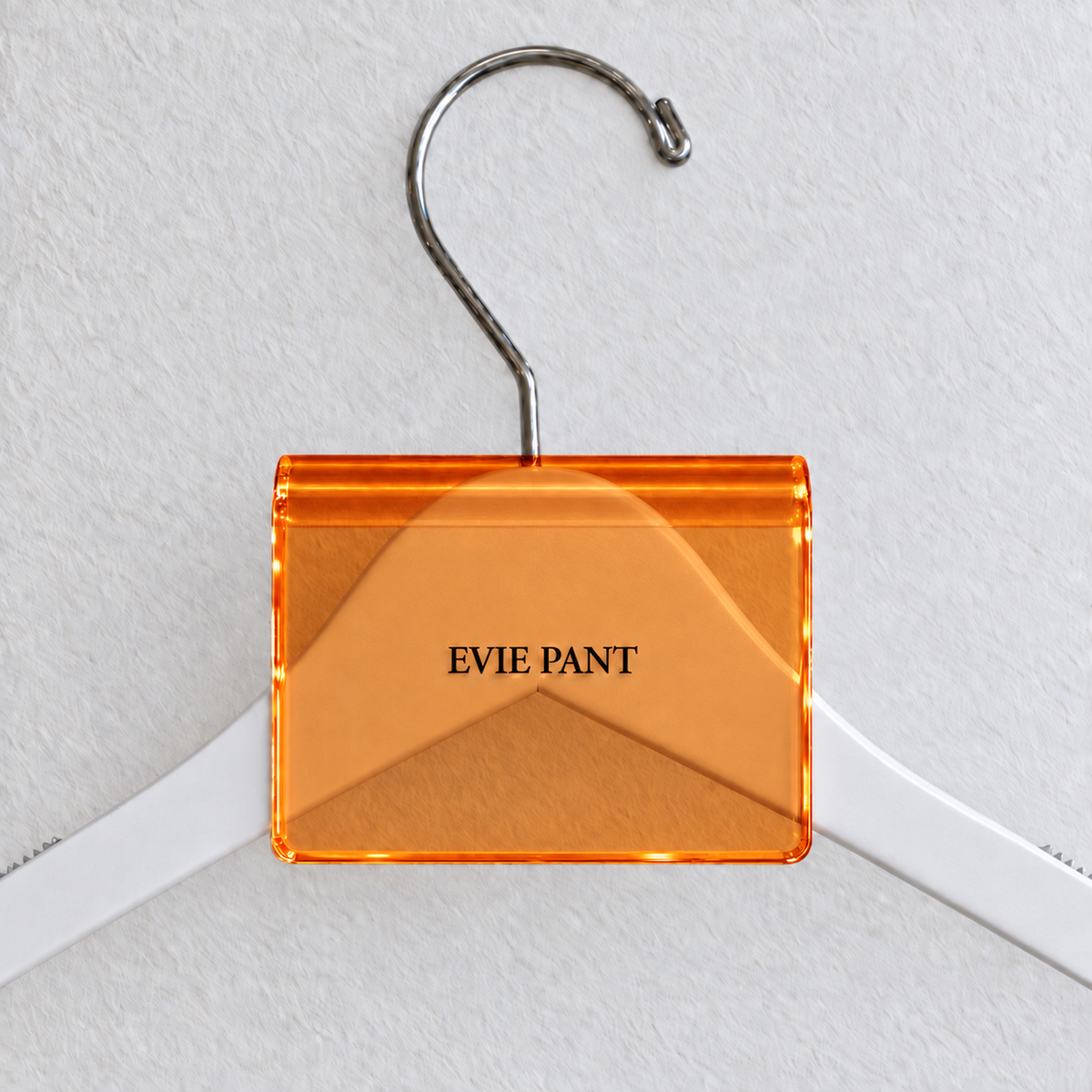 Orange acrylic hanger sign clip resting on the rounded crown of a white wooden hanger, with example EVIE PANT print