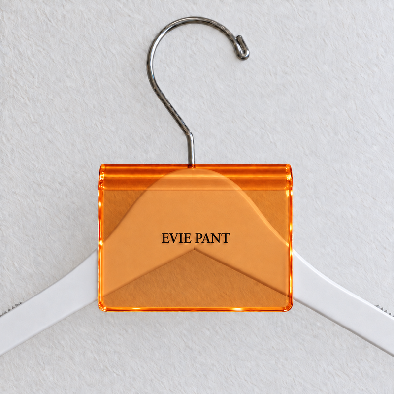 Orange acrylic hanger sign clip resting on the rounded crown of a white wooden hanger, with example EVIE PANT print