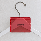 Red acrylic hanger sign clip resting on the rounded crown of a white wooden hanger, with example EVIE PANT print