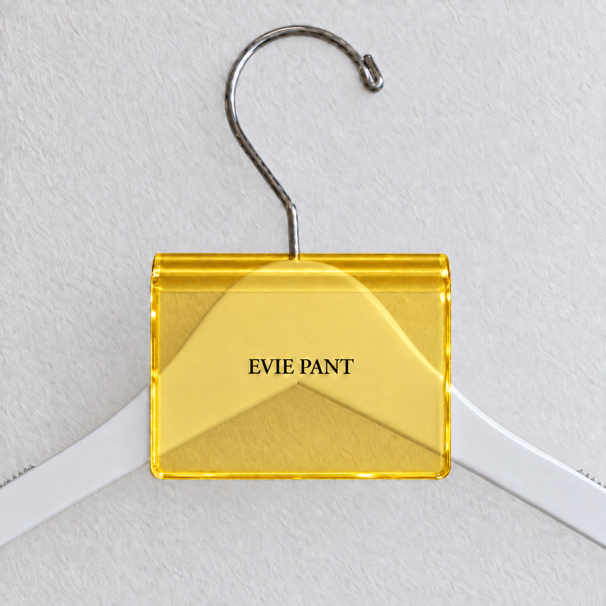 Yellow acrylic hanger sign clip resting on the rounded crown of a white wooden hanger, with example EVIE PANT print