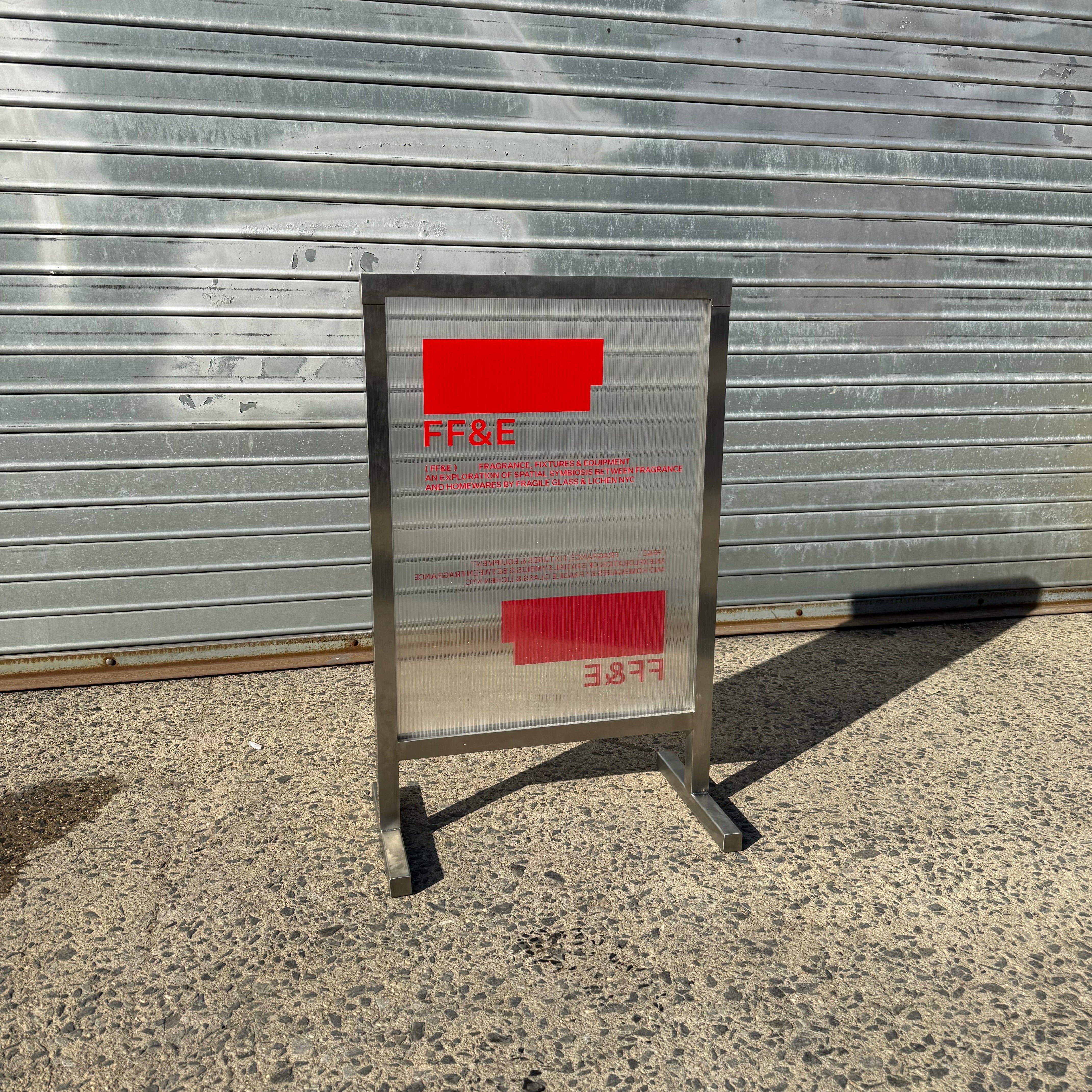 Metal sign with red and white text against a corrugated metal wall.