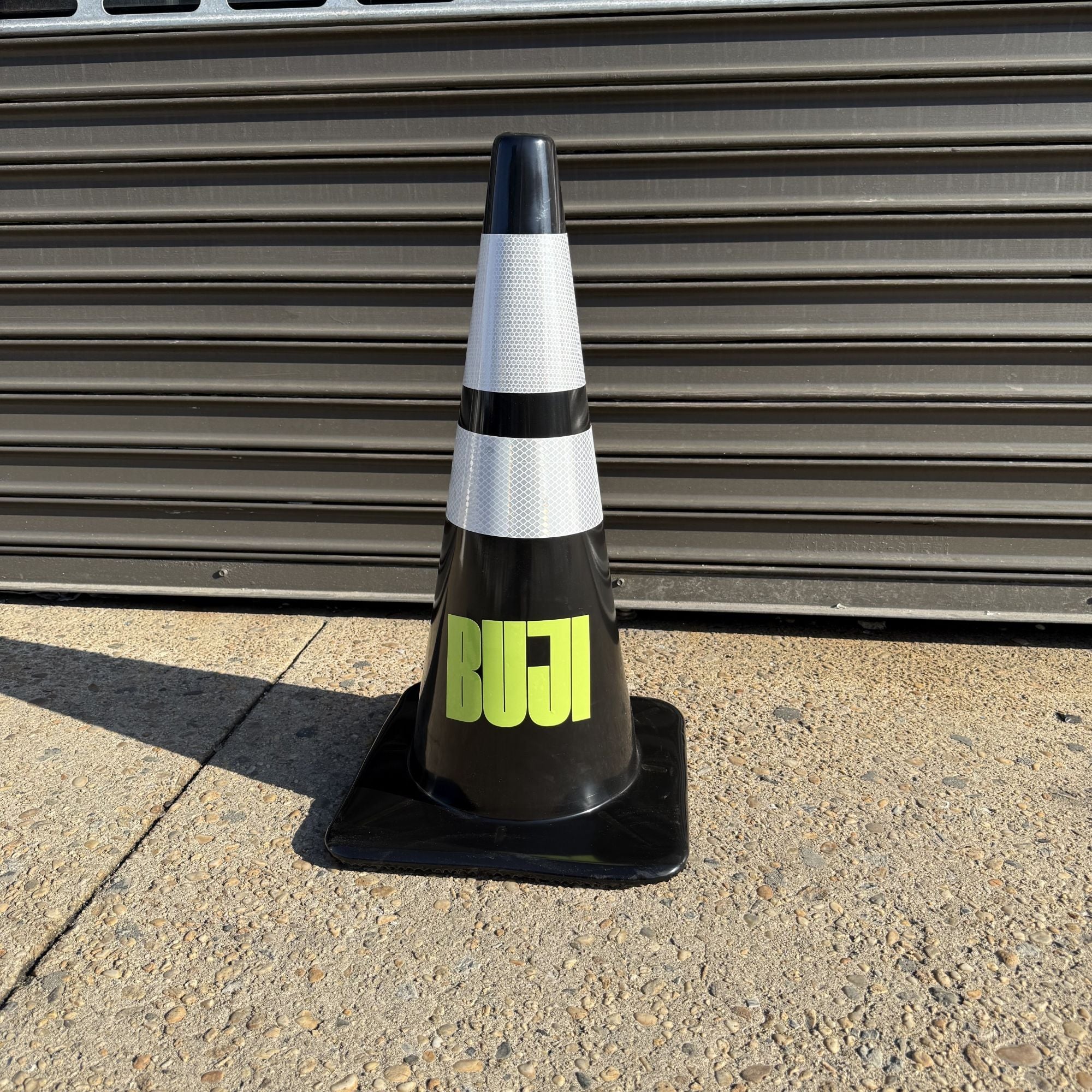 Black traffic cone with 'Bull' written on it against a corrugated metal background