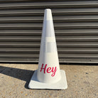 White traffic cone with 'Hey' written on it against a metallic background