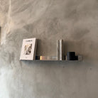 Metallic shelf against a textured gray wall with a book and small decorative item.