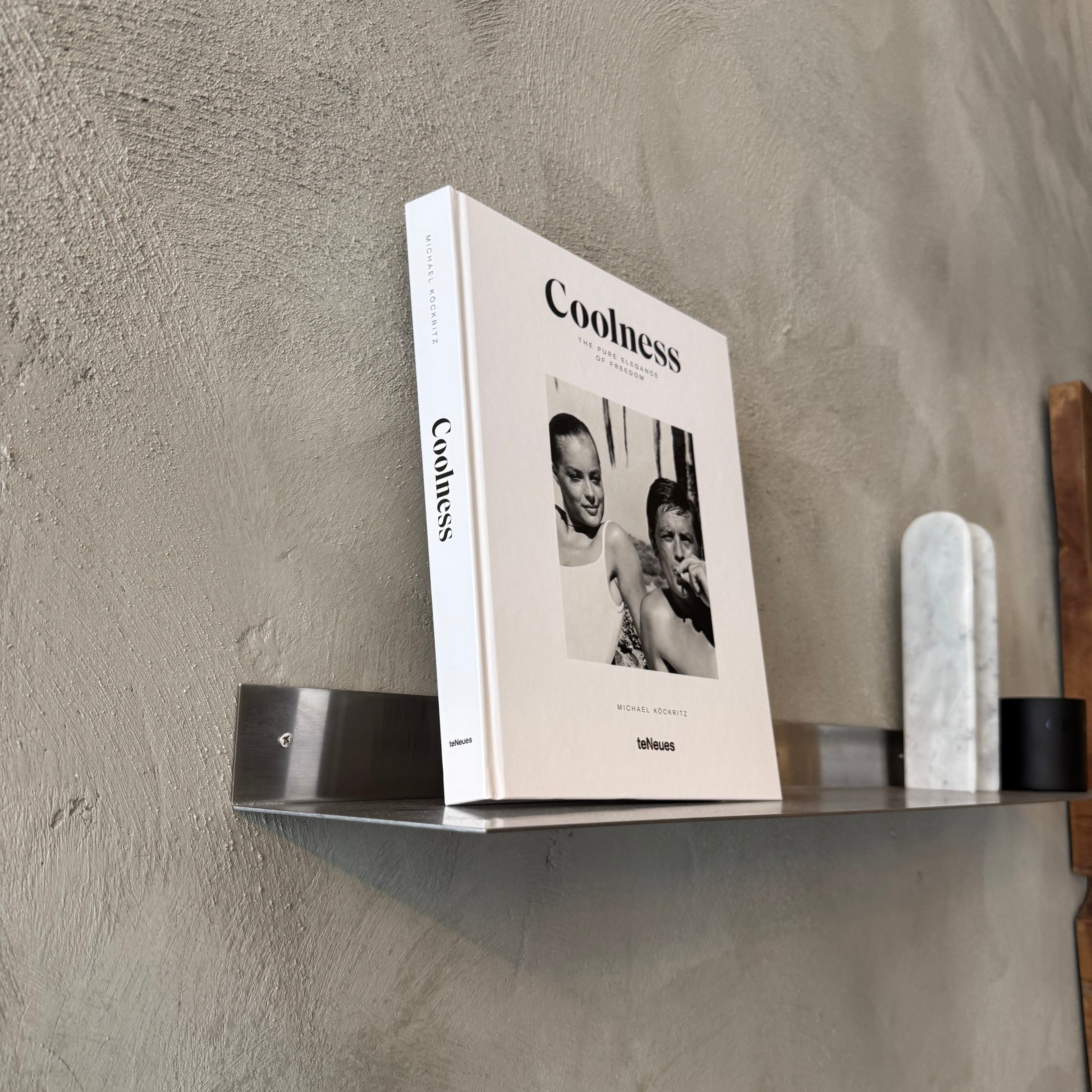 Book titled 'Coolness' on a wall-mounted shelf against a gray concrete wall.