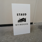 White sign with 'STAUD' and 'ST REGIS' text on a gray floor against a beige wall.
