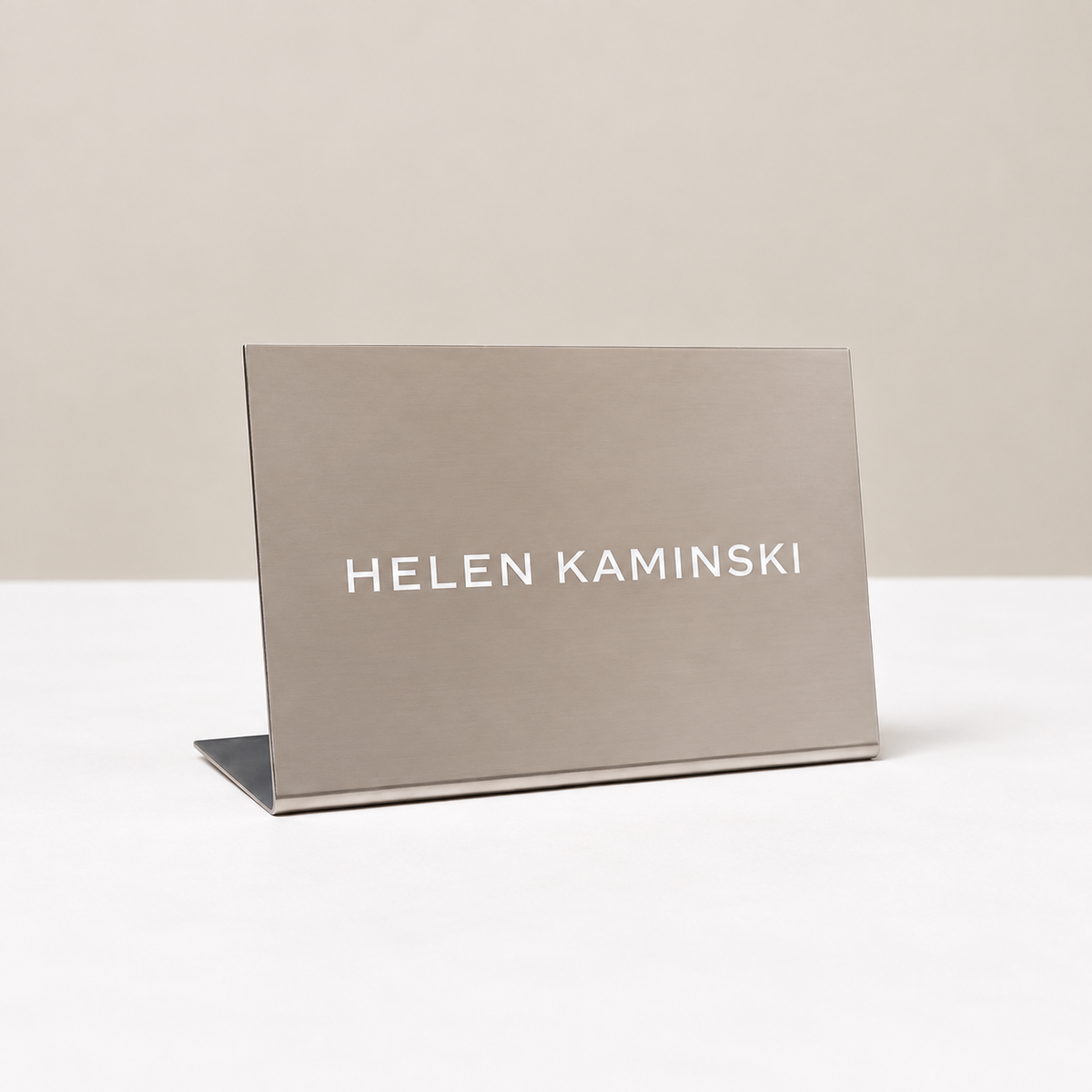 Landscape stainless steel tabletop stand with white Helen Kaminski lettering.