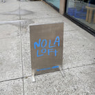 Stainless steel upright sign with blue Nola Loft lettering and an arrow.